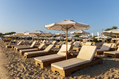 Güzel tropikal gün batımı. Plajdaki güneş sakin suların üzerinde sıcak ve rahatlatıcı bir parıltı yayarken, şemsiyeler gölge oluşturuyor. Güneşin doğuşu dinlenme tesisi