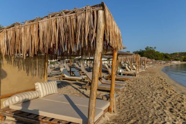 Güzel tropikal gün batımı. Plajdaki güneş sakin suların üzerinde sıcak ve rahatlatıcı bir parıltı yayarken, şemsiyeler gölge oluşturuyor. Güneşin doğuşu dinlenme tesisi