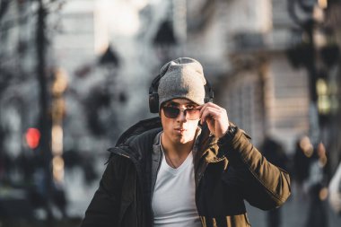 Yakışıklı, gülümseyen, yün şapkalı, güneş gözlüklü ve kulaklıklı genç adamın portresi.