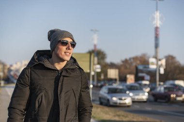 Soğuk kış gününde Yünlü Şapkalı ve güneş gözlüklü yakışıklı genç adam şehirde dikiliyor.