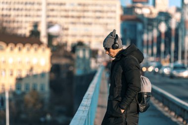 Yakışıklı, gülümseyen, yün şapkalı, güneş gözlüklü ve kulaklıklı genç adamın portresi.