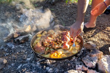 Vahşi doğada kamp yaparken kamp ateşinde yemek pişiren eller.