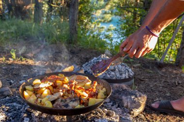 Açık havada kamp yaparken kamp ateşinde yemek pişiren eller..