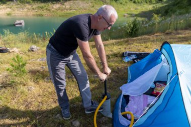 Kamp gününde bir adam çadırda şişme yatak şişiriyor. Turizm, seyahat ve macera konsepti.