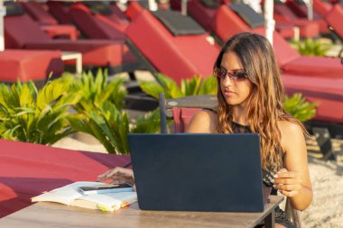 Genç bir kadın çalışmak ve çalışmak için sahilde dizüstü bilgisayar kullanıyor..