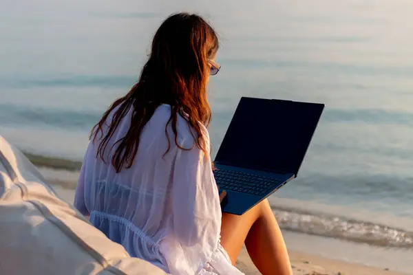Güzel bir sahilde dizüstü bilgisayarıyla çalışan bir kadın.