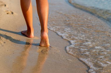 Sahilde yürüyen dişi bacaklar ve ayaklarına değen deniz köpüğü.