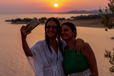 Mutlu bekar anne ve kızı yazın gün batımında selfie çekiyorlar.