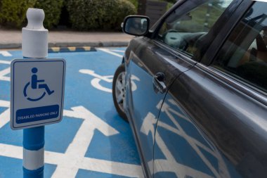 Park yerindeki engelliler için tekerlekli sandalyeye park eden gri araba..