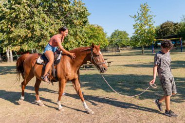 Genç bir erkek eğitmen, çiftlikte ata binen bir kıza liderlik ediyor..