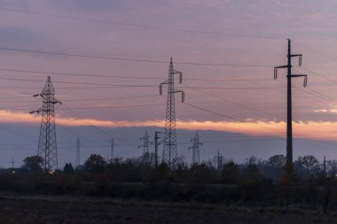 Gün batımında yüksek voltajlı elektrik hatları. Gelecekte, elektrik kıtlığı olacak. Yüksek fiyatlar yüzünden çaresiz insanların elektriğe verecek paraları yok.