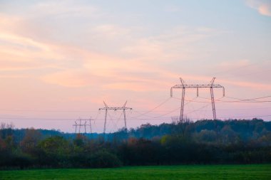 Gün batımında yüksek voltajlı elektrik hatları. Gelecekte, elektrik kıtlığı olacak. Yüksek fiyatlar yüzünden çaresiz insanların elektriğe verecek paraları yok.