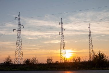 Gün batımında yüksek voltajlı elektrik hatları. Gelecekte elektrik sıkıntısı olacak. Yüksek fiyatlar yüzünden çaresiz insanların elektriğe verecek paraları yok.