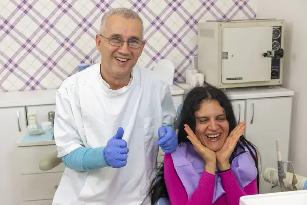 Hasta takımı mutlu bir şekilde gülümsüyor ve dişçiler onaylıyor. Mutlu hastalar ve dişçiler kavramı