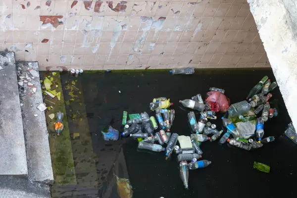 stock image Dirty muddy water in underpass in which plastic bottles float and garbage