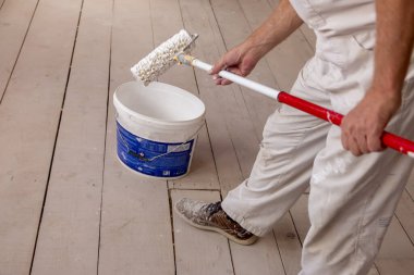 İnşaat işçisi boyacı elinde boya silindiri ve duvarları onarmak ve boyamak için kovalarca ürünü olan bir ev inşaatında çalışıyor. 