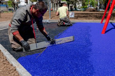 Belgrad, Sırbistan - 28 Nisan 2023: Yeni çocuk parkı yapım aşamasında. Çocuk oyun parkı için yumuşak lastik kırıntıları düzleştiren ve genişleyen mason bir el. Güvenlik için lastik yüzey.