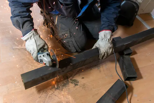 stock image The hands of the master saw the metal bars with a grinder. Metal works. Close up