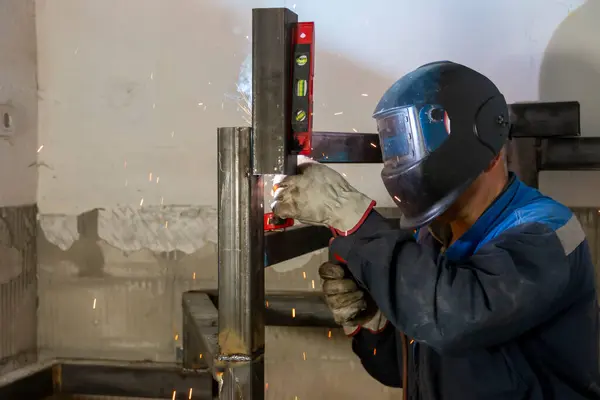 stock image An experienced man   using a spirit level and welding a seam on a spiral staircase at a construction site.