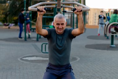 Olgun bir adam spor salonunda çalışıyor ve sağlıklı ve aktif bir hayat sürüyor. Ekipmanlı açık hava spor alanı, spor tesisleri, esneme, kardiyo ve fiziksel aktivite.