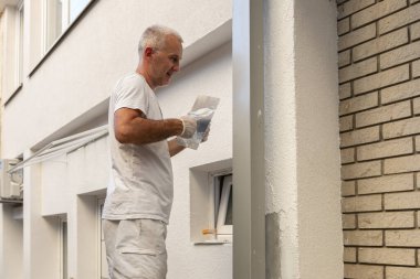 Construction worker applying final decorative facade plaster paste. Home renovation. Builders apartment improvement or restoration works. clipart