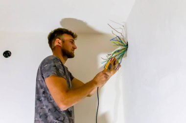 Elektrikçi, elektrik hattındaki kablo bağlantısını inceliyor. İnşaat alanındaki kanaldan teknisyen teli çekiyor. Çalıştırıcı çalışıyor, bağlantı kablolarını inceliyor.