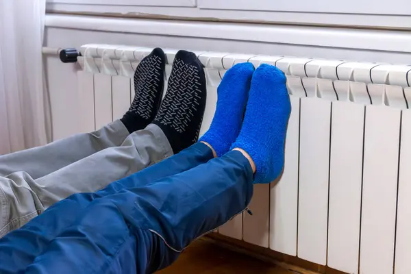 Bir çift pamuklu çorap giyen bir adam ve genç kış vakti radyatörün önünde soğuk ayakları ısıtıyorlar. Evde elektrikli ya da gazlı ısıtıcı var. Vücudun bir parçası, seçici odaklanma.