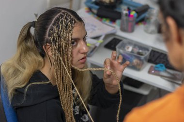 Bir stilistin kızı Senegalli saç örgülerini evinde yaptırıyor. Senegal örgülü güzel bir kızın portresi. Senegal örgülerine hazırlık kavramı..