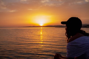 Güzel bir gün batımında sahilde oturan siluet kız. Yalnız kadın gün batımında iskelede 