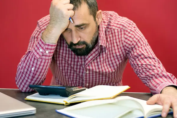 Başını tutan ofiste kırmızı ve beyaz gömlekli hayal kırıklığına uğramış sakallı işadamının portresi.