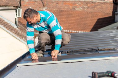 Roofer çatıda metal levha monte eder. İnşaat işçileri - yeni çatı montajı. Çatı araçları.