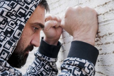 Anksiyete muzdarip genç depresif adam ve sefil duygu elleri ile yüzünü kaplayın ve duvara yaslanmış ağlamak