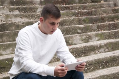 Beyaz yakışıklı genç adam merdivenlerde oturan ve tabletini kullanarak