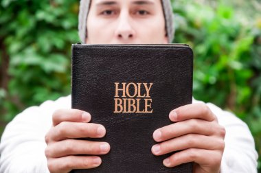 Parkta genç yakışıklı adam Kutsal kitap okurken Tanrı'ya dua ediyor. İnanç, maneviyat ve din kavramı.