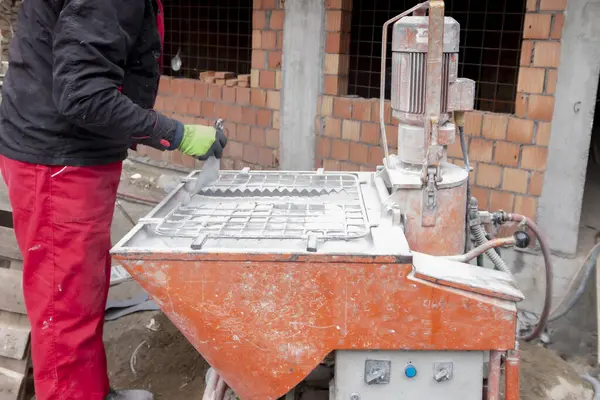 Kuru alçıyı suyla karıştırmak ve otomatik olarak bitmiş alçıyı beslemek için otomatik karıştırıcı. Bir işçi zıpzıpa bir torba kuru sıva döker..