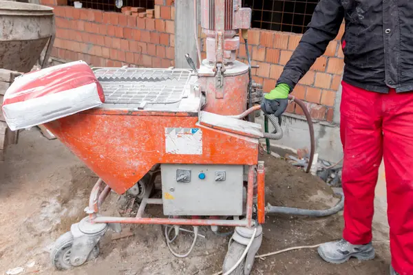 Kuru alçıyı suyla karıştırmak ve otomatik olarak bitmiş alçıyı beslemek için otomatik karıştırıcı. Bir işçi zıpzıpa bir torba kuru sıva döker..