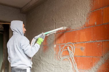 Binanın içindeki duvarlara makine ile alçı yapıştırma işlemi. Sıvacı yeni evin duvarlarına sıva fırlatıyor..  