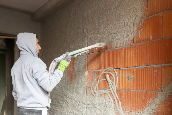 Binanın içindeki duvarlara makine ile alçı yapıştırma işlemi. Sıvacı yeni evin duvarlarına sıva fırlatıyor..  