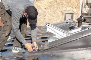 Zanaatkar tavan penceresini metal levha ile kaplıyor. Çatı pencereleri alüminyum çarşafla kaplı bir çatıya monte edilmiş. Bir çatı ustası ve pencere ustası.