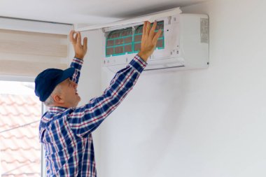 Tamirci bir eve klima takıyor ya da tamir ediyor. Bir teknisyen temizleme için klimanın hava filtresini kaldırıyor.. 