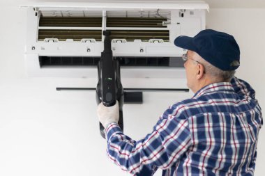 Evde klimayı temizlemek için elektrikli süpürge kullanan olgun bir adam. Klimanın bakımı