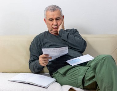 Kağıt dökümanlarda beklenmedik haberler okuyan orta yaşlı bir adam. Şaşırmış ve şaşırmış durumda: yüksek fatura faturası, borç bildirimi, kötü mali rapor, para sorunu