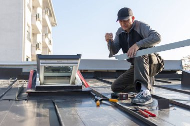 Çatı ustası bir işçi, metal bir levhayı katlamayı büyük düz bir penseyle bitiriyor. Çatı ustası ve pencere ustası. İnşaat konsepti altında ev geliştirme 