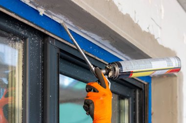 Delikanlı eli sprey tabanca kullanıyor ve boşluğu inşaat köpüğüyle dolduruyor. İnşaat işçisi yalıtım için PVC penceresine genişletilebilir köpük koyuyor. Yakın çekim.. 