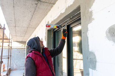 Delikanlı eli sprey tabanca kullanıyor ve boşluğu inşaat köpüğüyle dolduruyor. İnşaat işçisi yalıtım için PVC penceresine genişletilebilir köpük koyuyor. Yakın çekim.. 