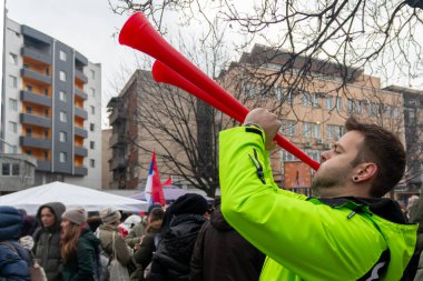 Kragujevac, Sırbistan 14 Şubat 2025 - Genç yakışıklı bir adam sokakta iki vuvuzela üflüyor. Barışçıl protestolar. Öğrenciler hükümet yolsuzluğunu, rejimi ve değişim talebini protesto ediyorlar. 