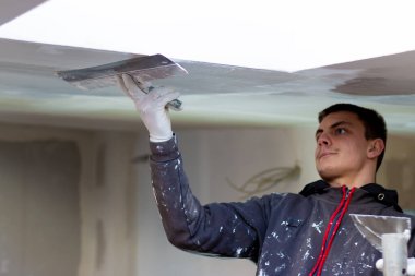 Alçıpan tavanına macun koyan bir adam. Plasterboard çarşafları için macun. Tadilat ve inşaat işleri. Ev geliştirmeleri.
