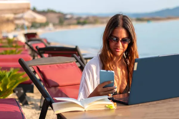 Kumsaldaki kahvede dizüstü bilgisayarda çalışan genç ve güzel bir kadın. Yaz tatilinde açık havada seyahat eden bir kadın. Serbest ve uzak çalışma
