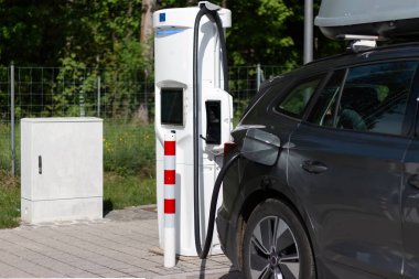 Elektrikli araba şarj istasyonunda. Batarya EV aracı fişe takıldı ve yenilenebilir enerji jenerasyonları güneş paneli ve rüzgar türbininden elektrik alıyor. Araç şarj ediliyor.