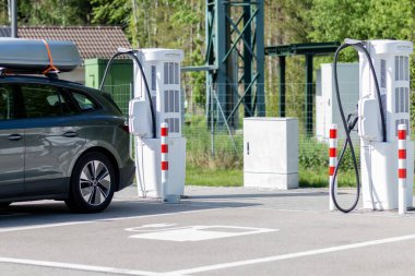 Yeşil çevredeki şarj istasyonunda elektrikli araba. Batarya EV aracı fişe takıldı ve yenilenebilir enerji jenerasyonları güneş paneli ve rüzgar türbininden elektrik alıyor. Araç şarj ediliyor.